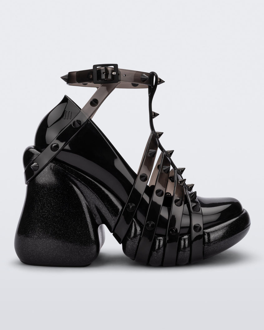 Side view of a black/clear Melissa Punk Love Heel with black straps fastening at a top ankle strap with spike details.