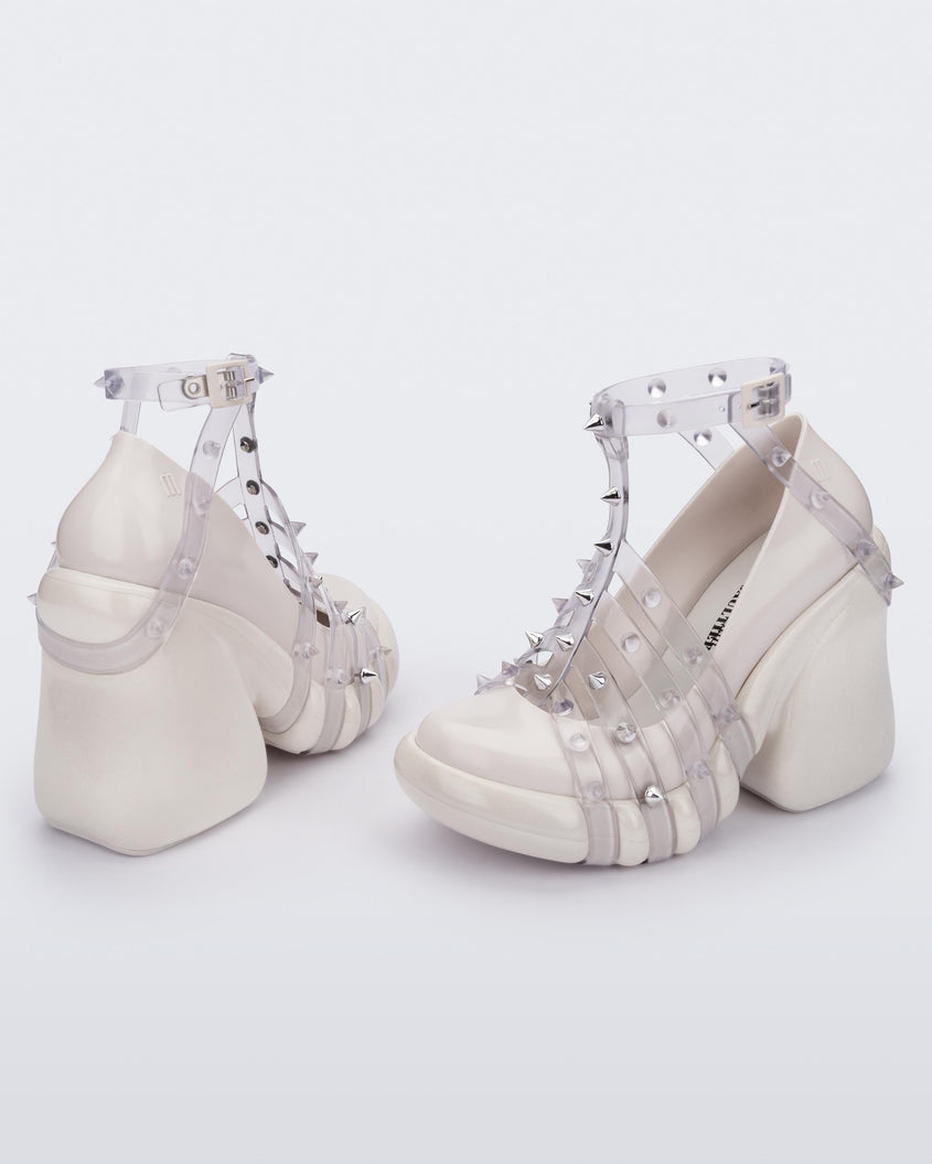 An angled side and back view of a pair of White/Clear Melissa Punk Love Heels with a white base and clear straps fastening at a top ankle strap with spike details.