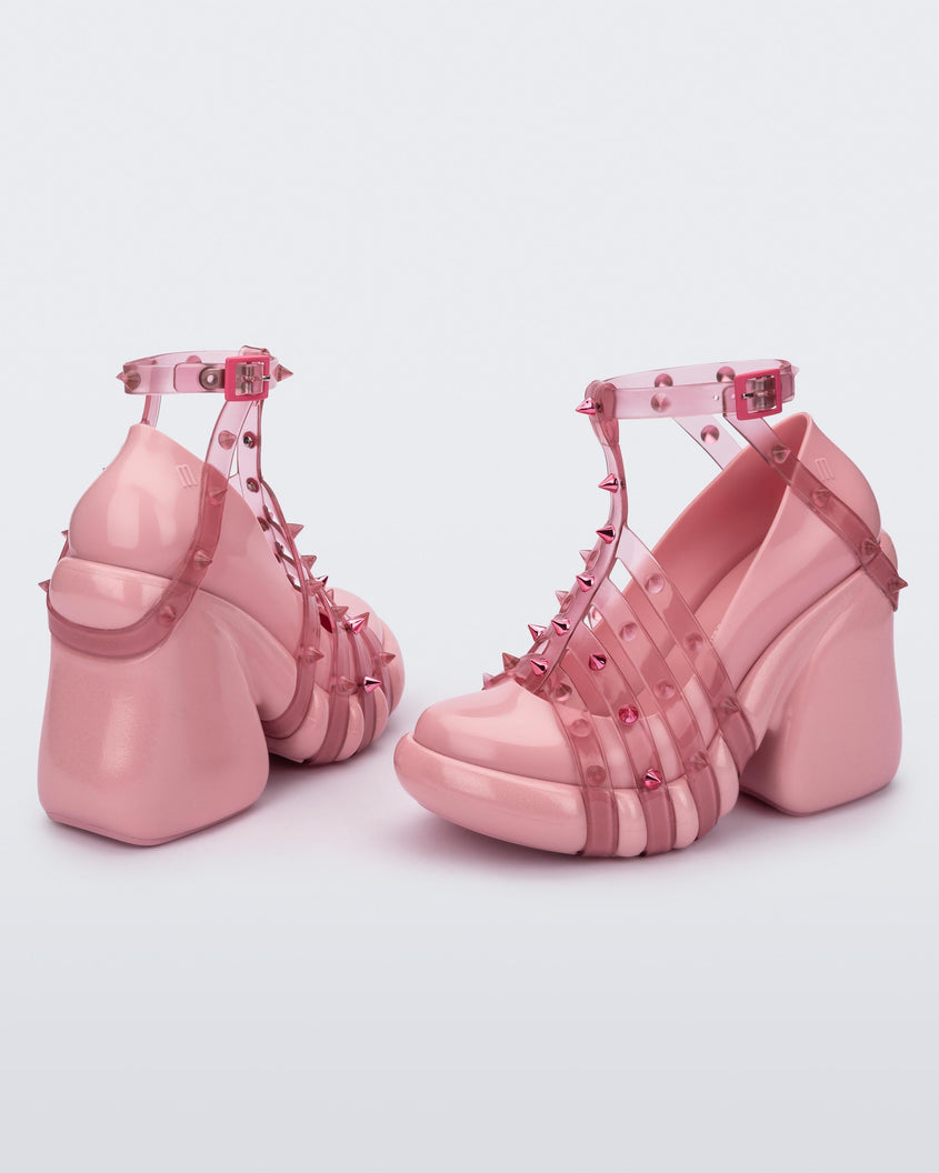 A side and back view of a pair of pink/transparent Melissa Punk Love Heels with pink straps fastening at a top ankle strap with spike details.