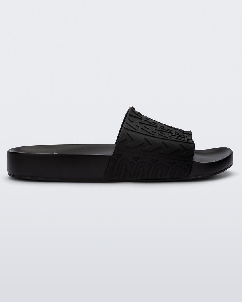 Side view of a black Melissa Slide with the Marc Jacobs logo across the front strap.