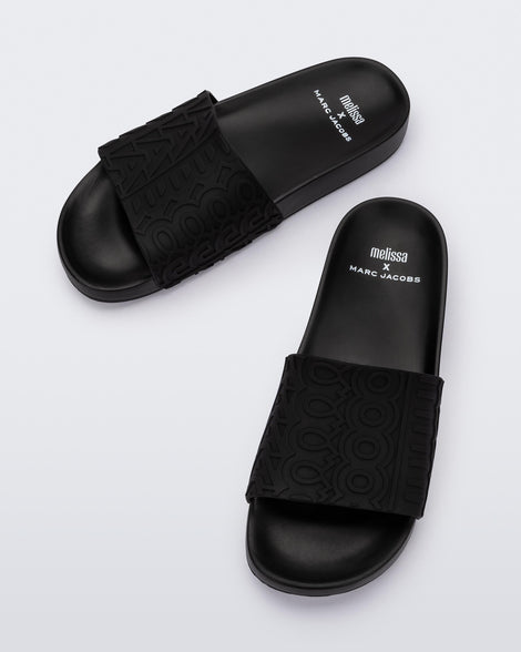 Top view of a pair of black Melissa Slides with the Marc Jacobs logo across the front strap.