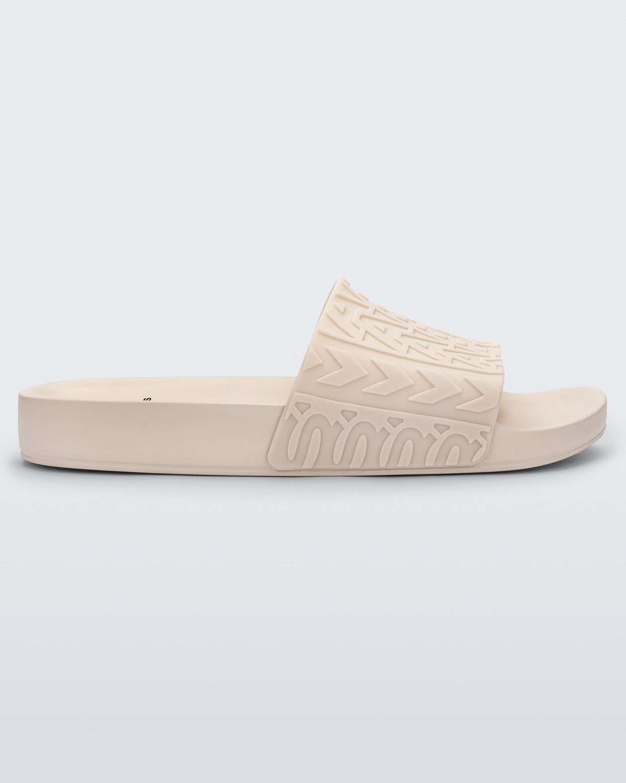 Side view of a beige Melissa Slide with the Marc Jacob's logo across the front strap.