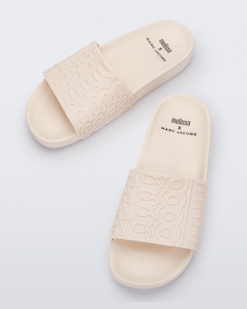 Top view of a pair of beige Melissa Slides with the Marc Jacob's logo across the front strap.
