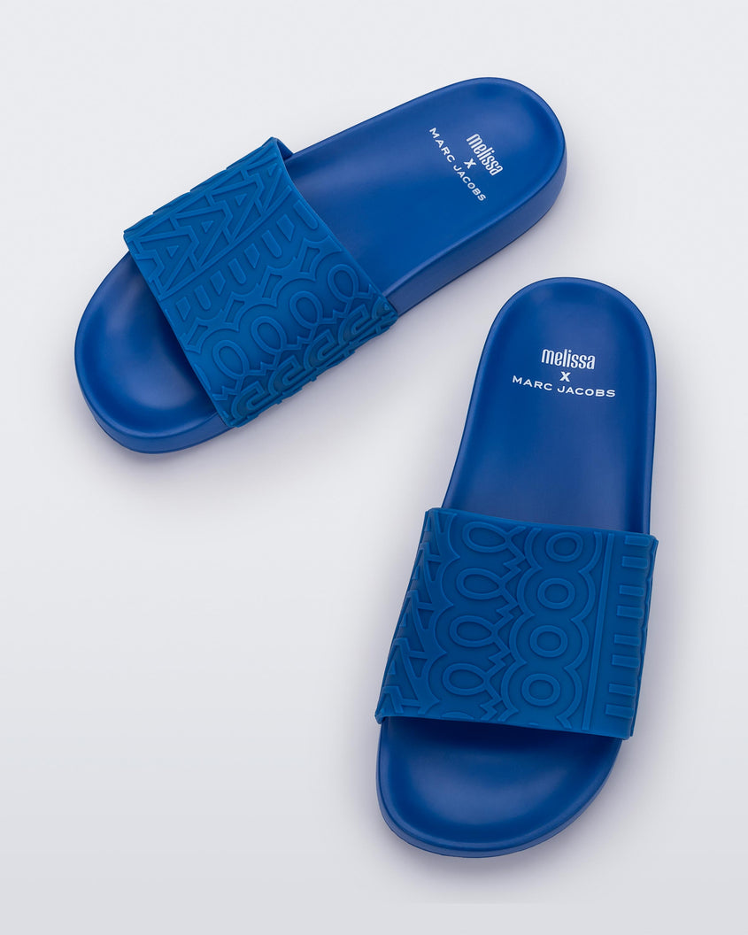 Top view of a pair of blue Melissa Slides with the marc jacob's logo across the front strap.