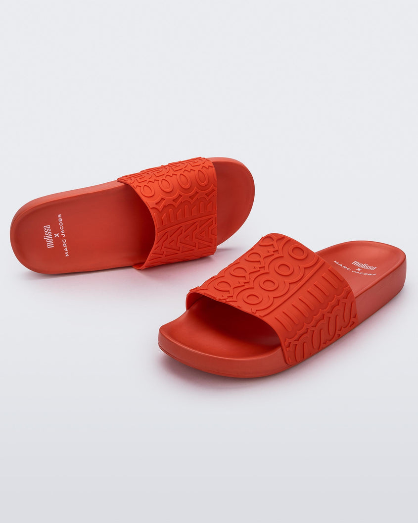 An angled front and top view of a red Melissa Slides with the Marc Jacobs logo across the front strap.