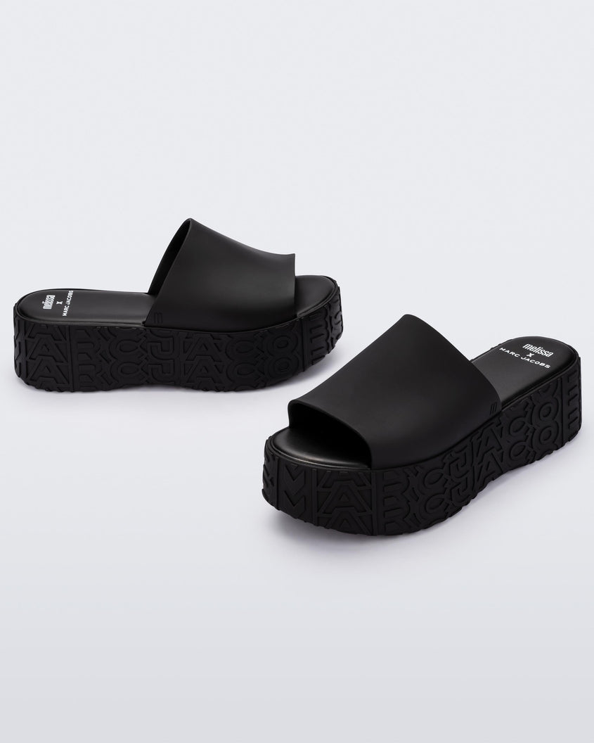 An angled front and side view of a pair of black Melissa Becky platform slides with the marc jacobs logo across the sole.