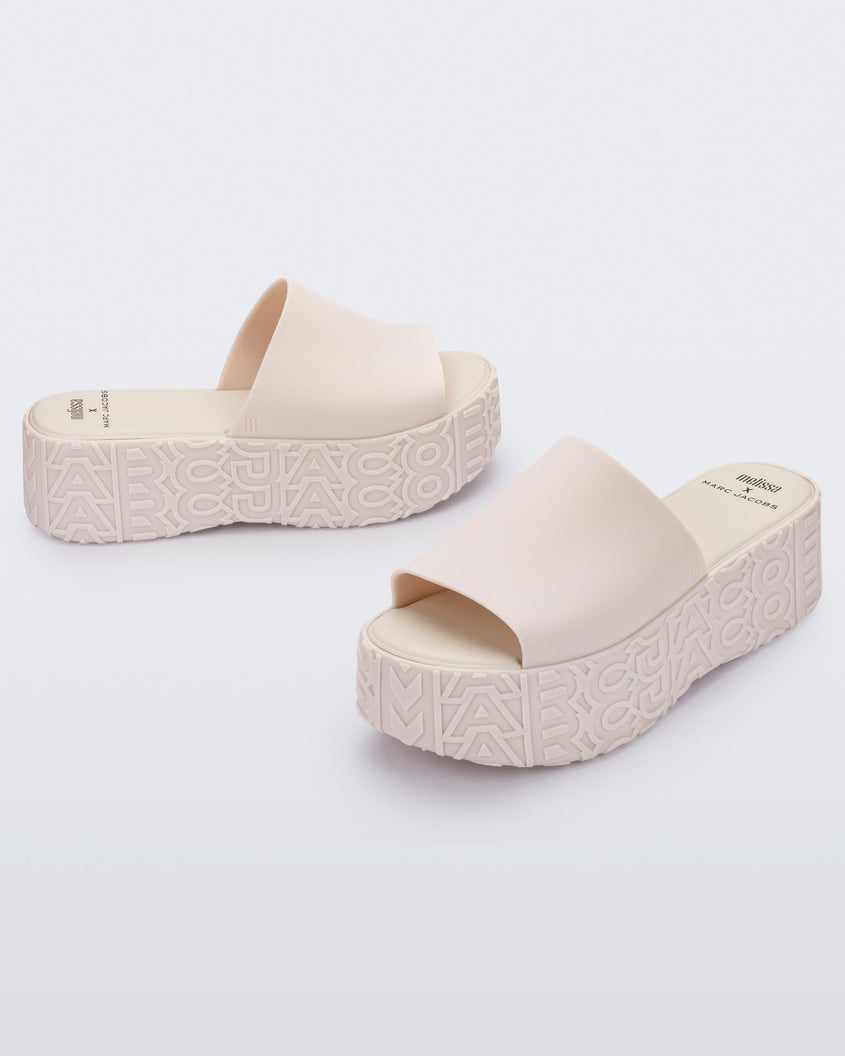 An angled side and front view of a pair of beige Melissa Becky platform slides with the Marc Jacob's logo across the sole.