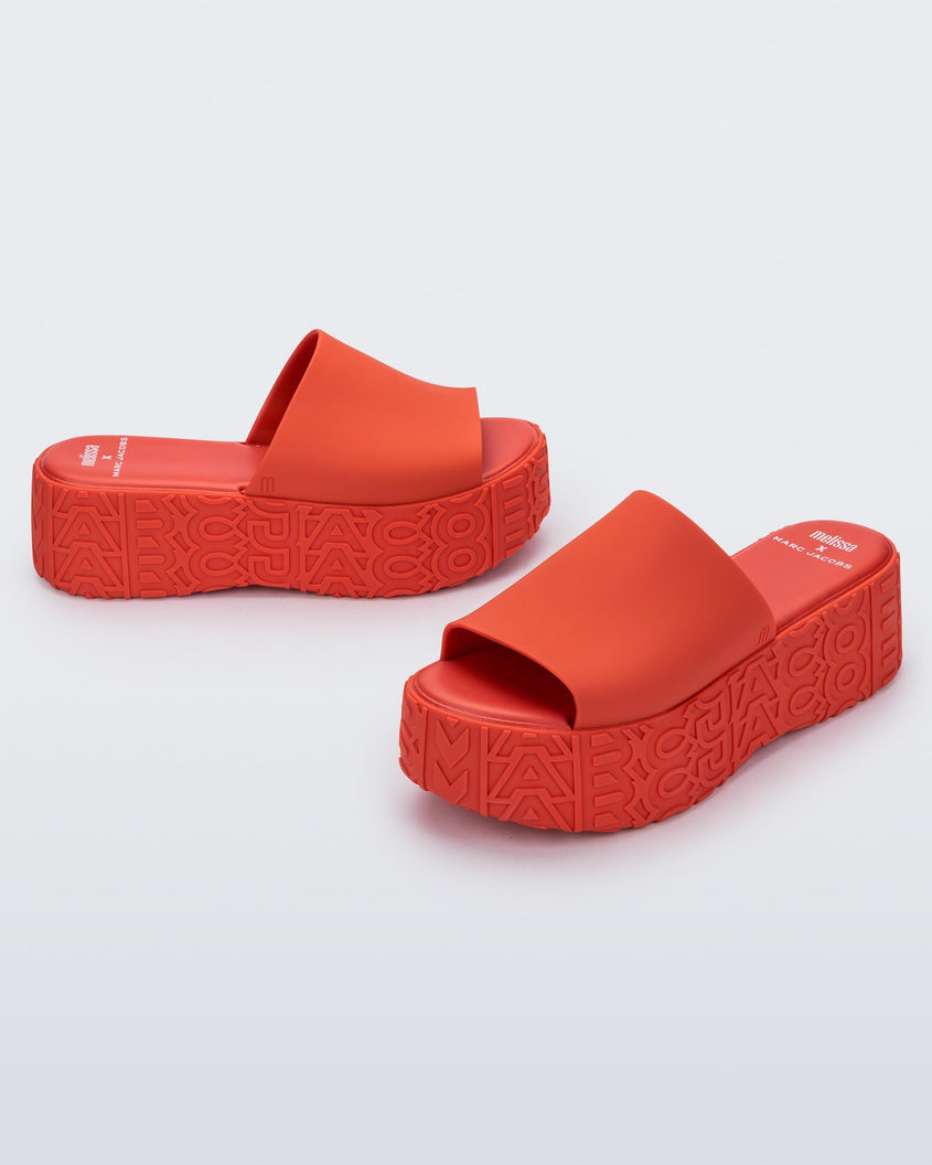 An angled front and side view of a pair of red Melissa Becky platform slides with the marc jacobs logo across the sole.