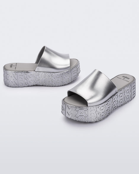 An angled front and side view of a silver Melissa Becky platform slides with the Marc Jacob's logo across the sole.
