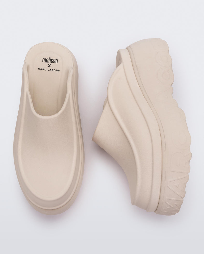 A top and side view of a pair of beige Melissa Clogs with the Marc Jacob's logo across the sole.