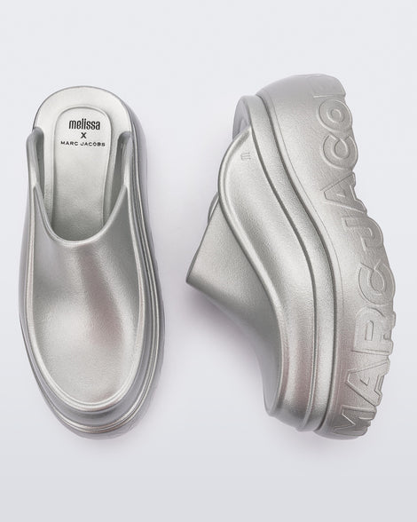 A top and side view of a pair of silver Melissa Clogs with the Marc Jacob's logo across the sole.