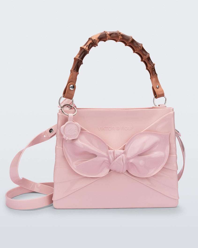 Front view of the Melissa Tie handag in pink with long shoulder strap, 3D bow detail on the front and natural colored bamboo shaped top handle.