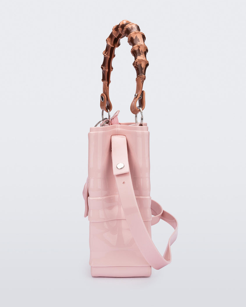 Side view of the Melissa Tie handag in pink with long shoulder strap, 3D bow detail on the front and natural colored bamboo shaped top handle.