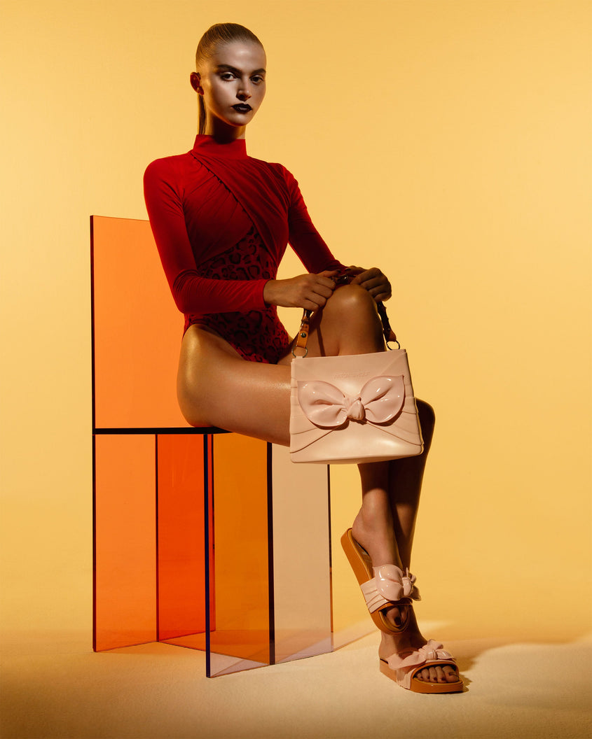 A model posing in a red bodysuit holding a Melissa Tie handbag in pink