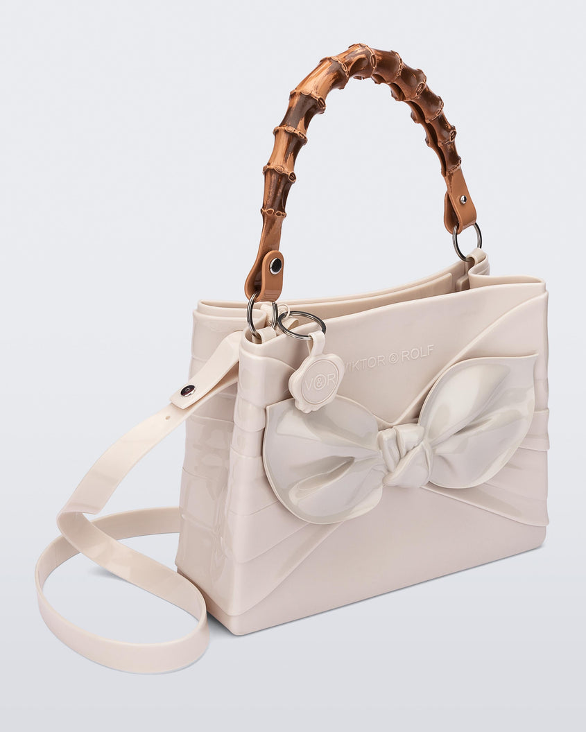 An angled side view of a beige Melissa Tie Bag with a bow detail on the front, two bamboo top straps and a beige shoulder strap.