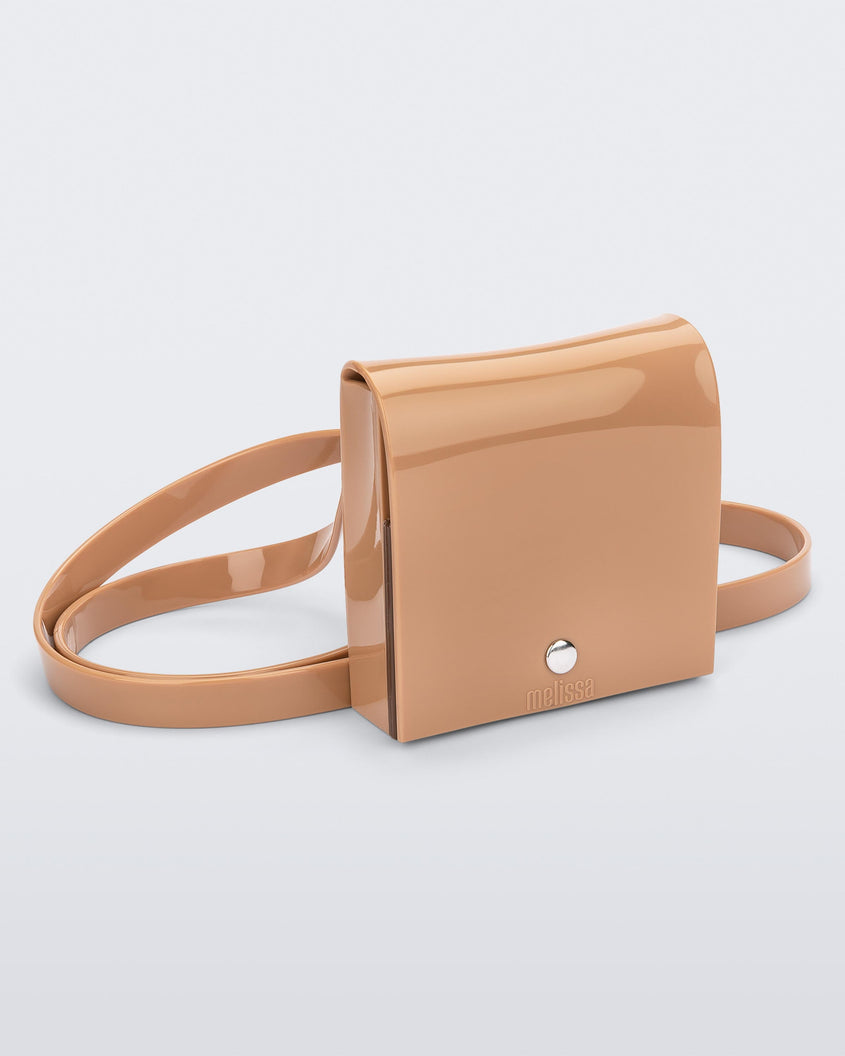 An angled front view of a beige Melissa Like It purse with a silver button and a Melissa logo on the front.