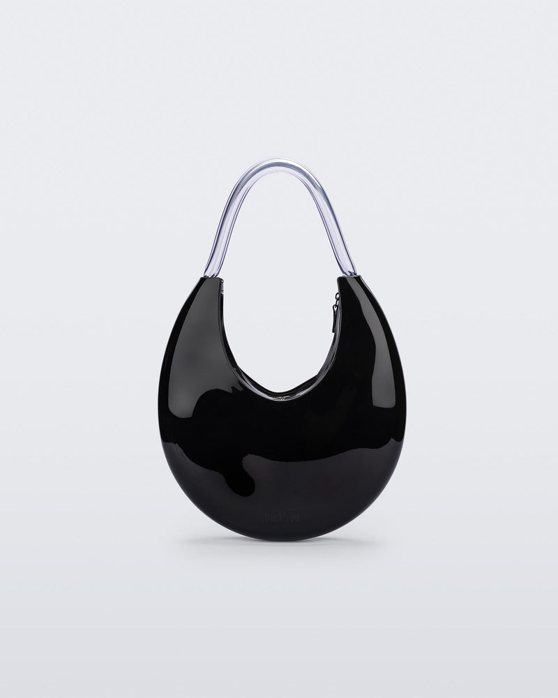 Front view of the Melissa Moon Handbag. The body of the bag is crescent shaped and is black with a top zipper closer. There is a short shoulder handle that is clear / transparent material.