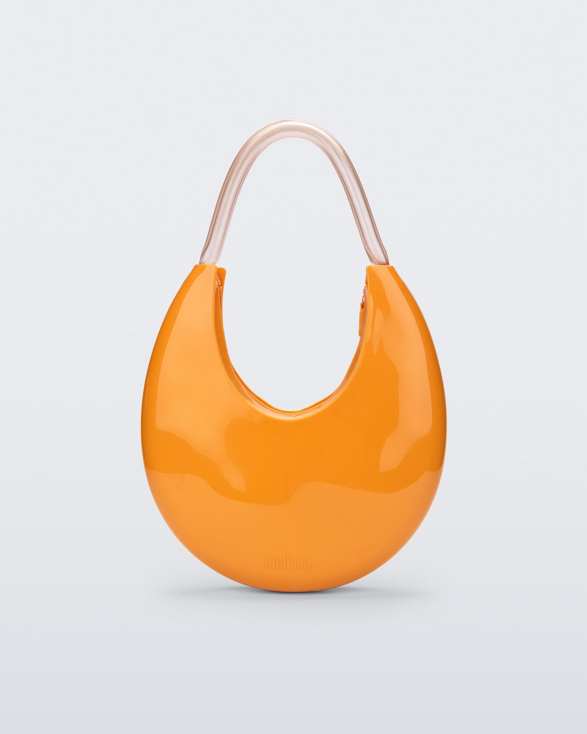 A front view of a orange/beige Melissa Moon Bag with a crescent shaped orange bag base and a clear beige top strap.