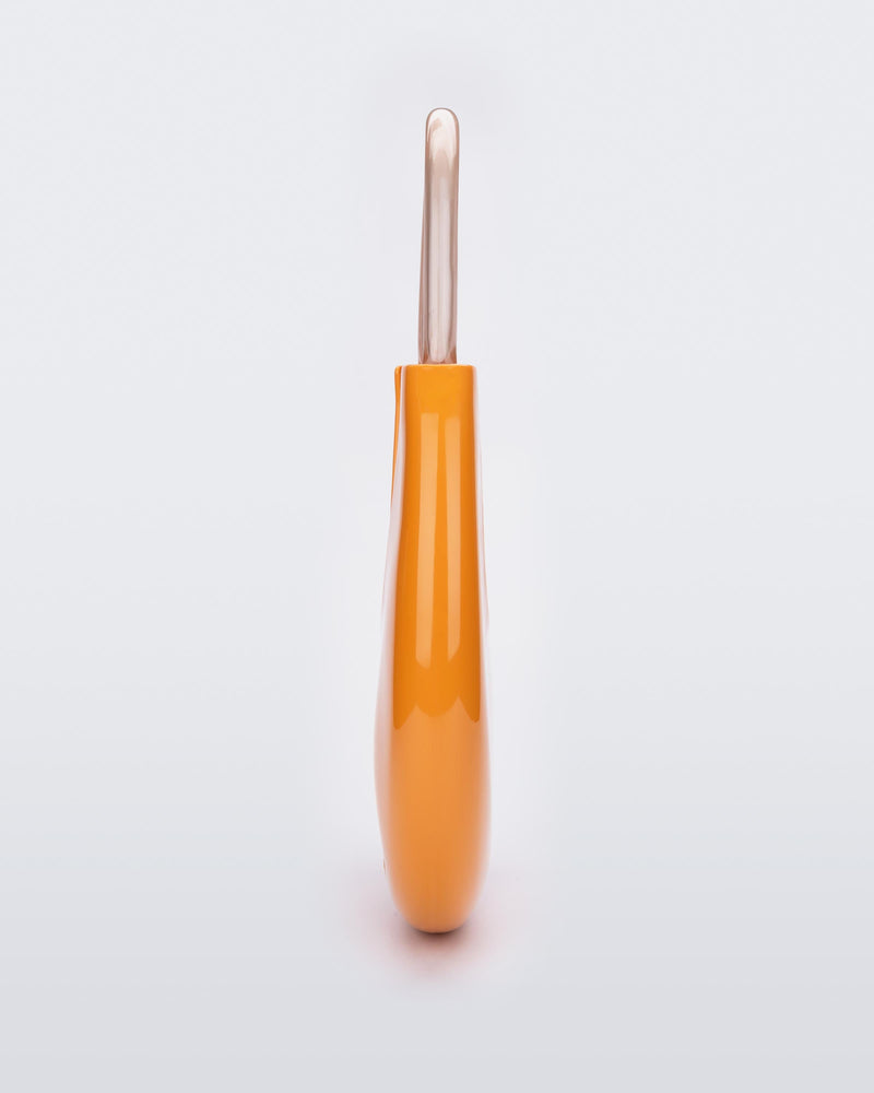 A side view of a orange/beige Melissa Moon Bag with a crescent shaped orange bag base and a clear beige top strap.