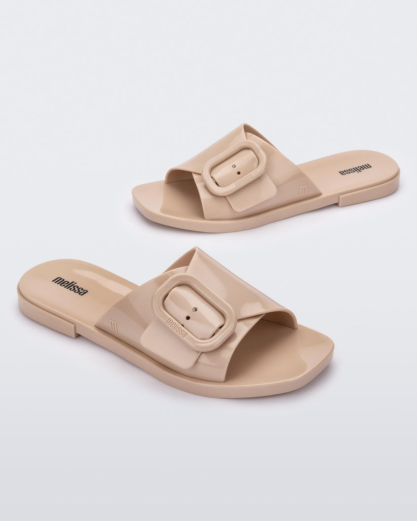 Side view of a pair of Beige Melissa Lislie slides with a buckle detail on the top strap.