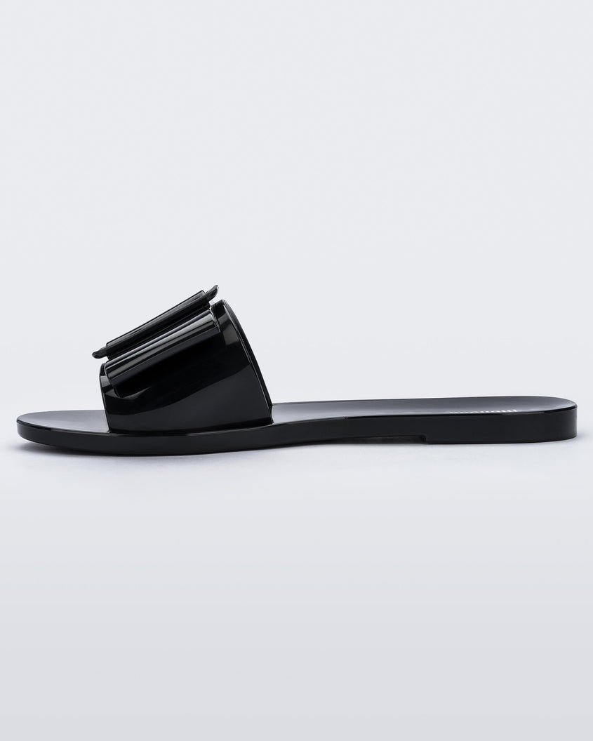 An inner side view of a black Melissa Babe slide with a buckle like bow detail on the front strap.