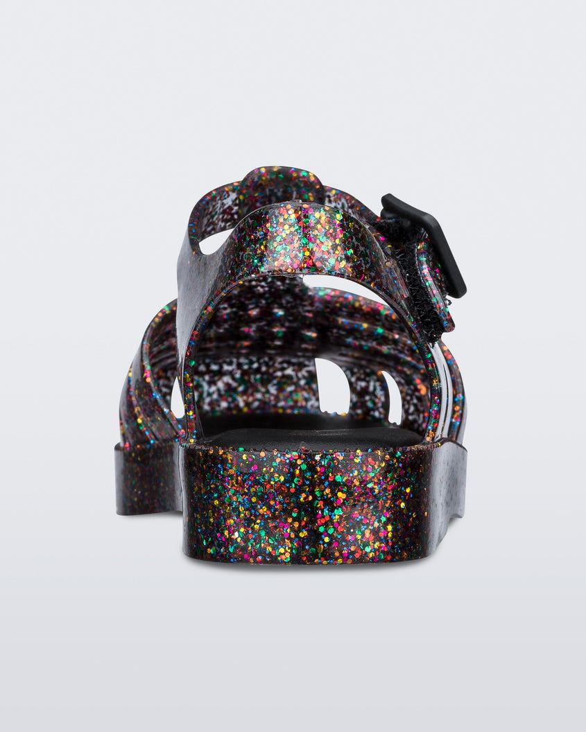 Back view of a Mixed Glitter Glass Mini Melissa Possession sandal with multiple multicolor glitter straps, black buckle and a multicolor glitter sole.