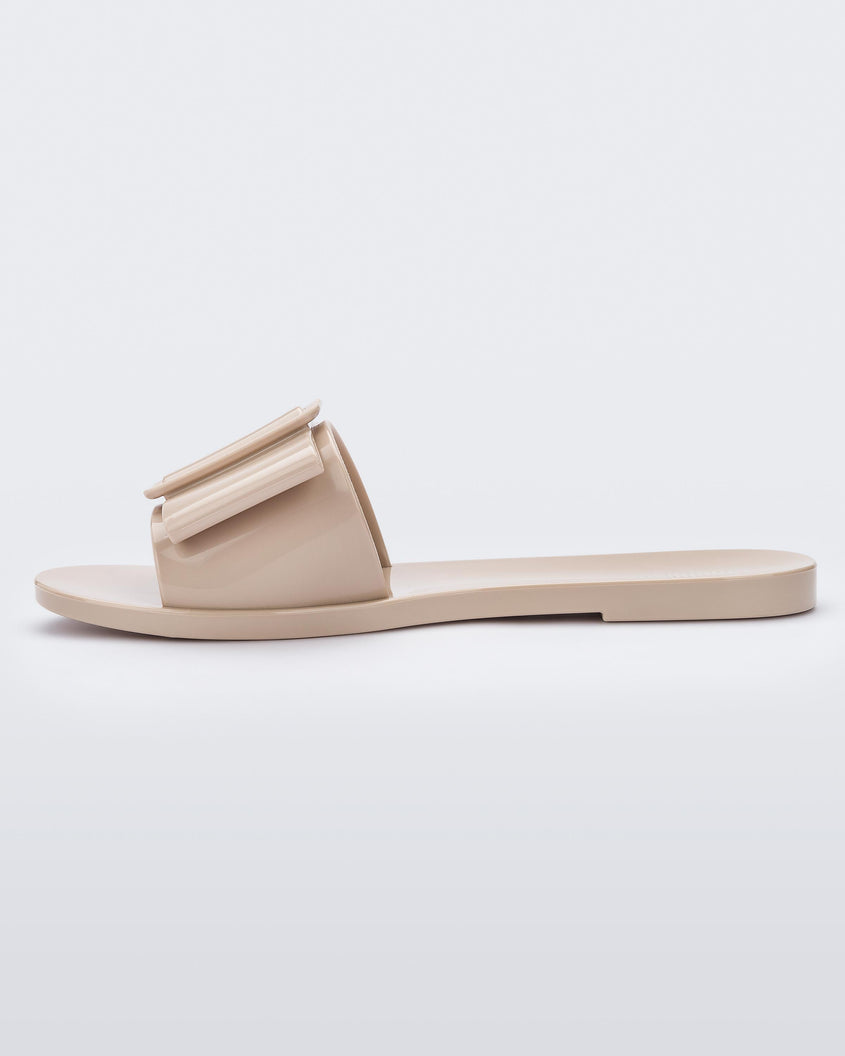 An inner side view of a Beige Melissa Babe slide with a buckle like bow detail on the front strap.