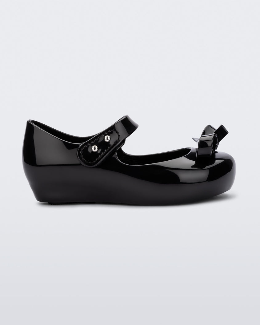 Side view of a black Mini Melissa Ultragirl Bow flat with a black base, top strap and black bow detail on the top.