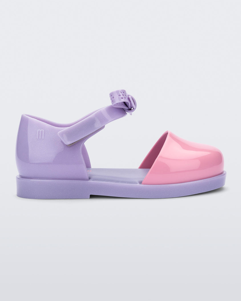 Side view of a Lilac/Pink Mini Melissa Amy sandal with a pink closed toe section and a back lilac strap with a lace like bow detail.