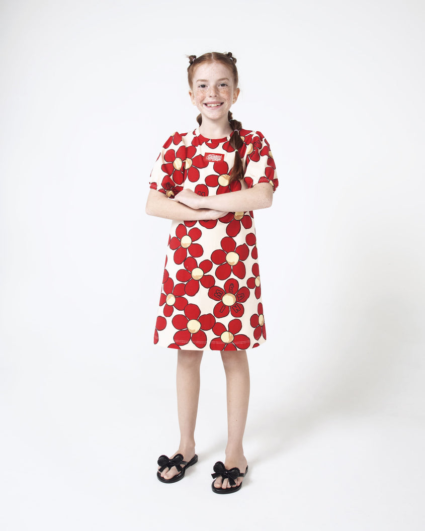 A model posing for a picture in a red and white floral dress, wearing a pair of Black Mini Melissa Slim flip flops with a lace like bow detail on the front straps.