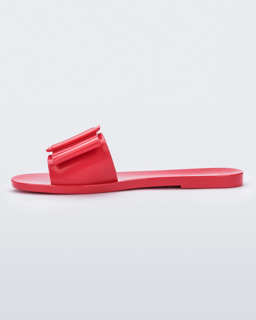 An inner side view of a red Melissa Babe slide with a buckle like bow detail on the front strap.