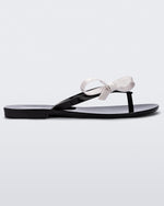 Side view of a black/white Melissa Harmonic Sweet flip flop with a black sole, straps and white bow on top.