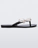 Side view of a black/white Melissa Harmonic Sweet flip flop with a black sole, straps and white bow on top.