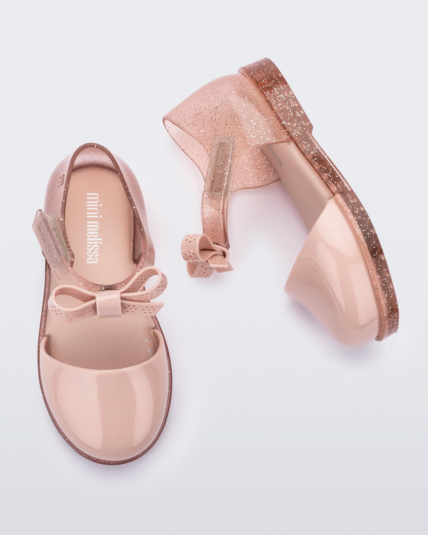 A top and side view of a pair of pink Mini Melissa Amy sandals with a pink closed toe section and a back pink glitter strap with a lace like bow detail.