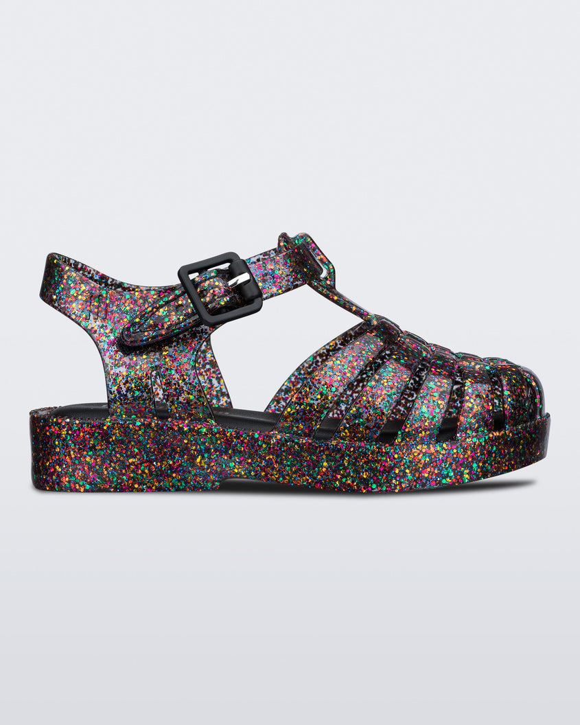Side view of a Mixed Glitter Glass Mini Melissa Possession sandal with multiple multicolor glitter straps, black buckle and a multicolor glitter sole.