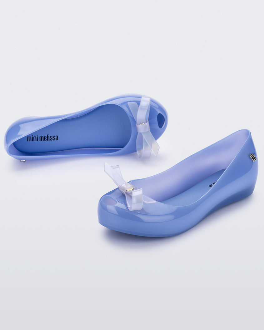 An angled side and top view of a pair of blue Mini Melissa Ultragirl Bow flats with a blue base and a white bow.