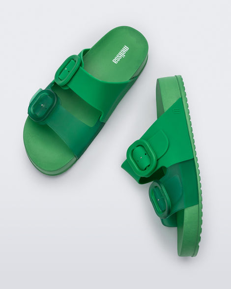 A top and side view of a pair of Green Melissa Cozy slides with two green and transparent green straps with a buckle detail.