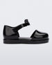 Side view of a Black Mini Melissa Amy sandal with a covered toe section and a single black strap with a lace like bow detail.