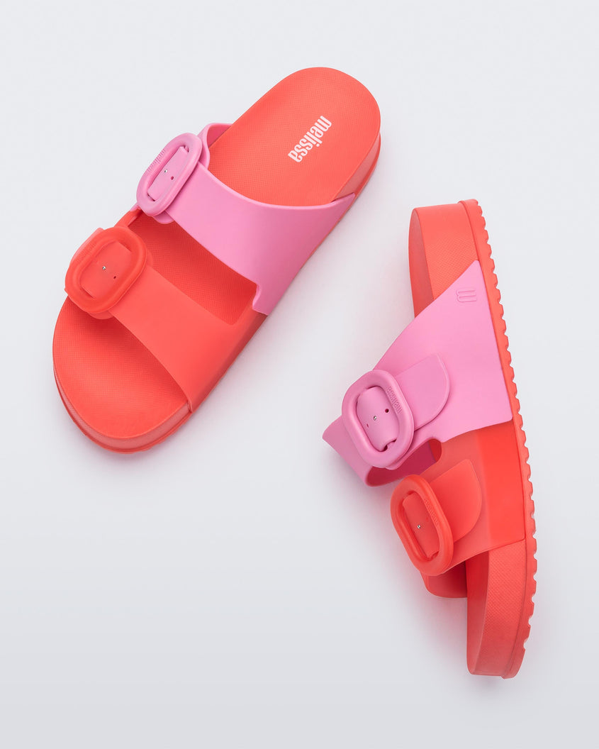 A top and side view of a pair of Red/Pink Melissa Cozy slides with two red and pink straps with a buckle detail.