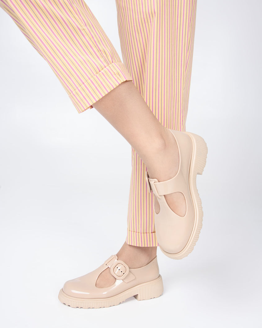 A model's legs in yellow striped pants, wearing a pair of beige Melissa Jackie loafers with two cut outs and a buckle detail strap.