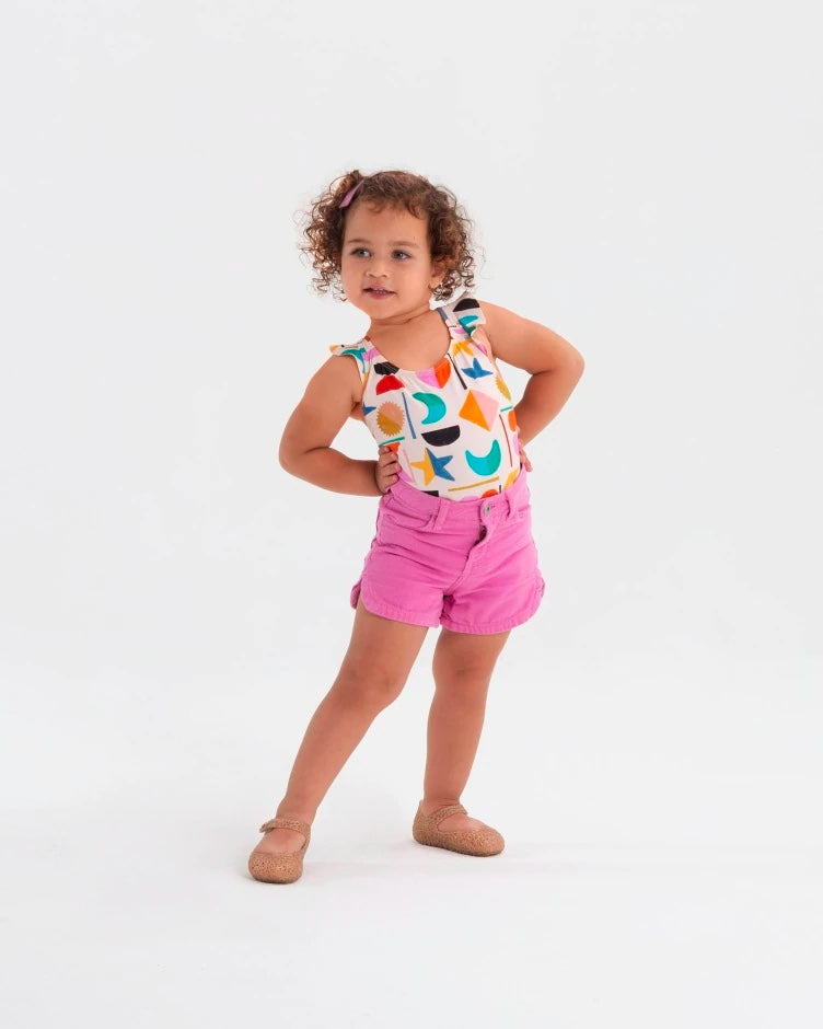 A child model posing in pink shorts and a colorful shirt wearing the Mini Melissa Campana beige glitter flats .