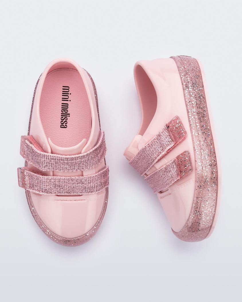 A top and side view of a pair of Pink/Pink Glitter Mini Melissa Beanny Bugs sneakers with a pink base, two shiny pink velcro straps and a pink glitter sole.
