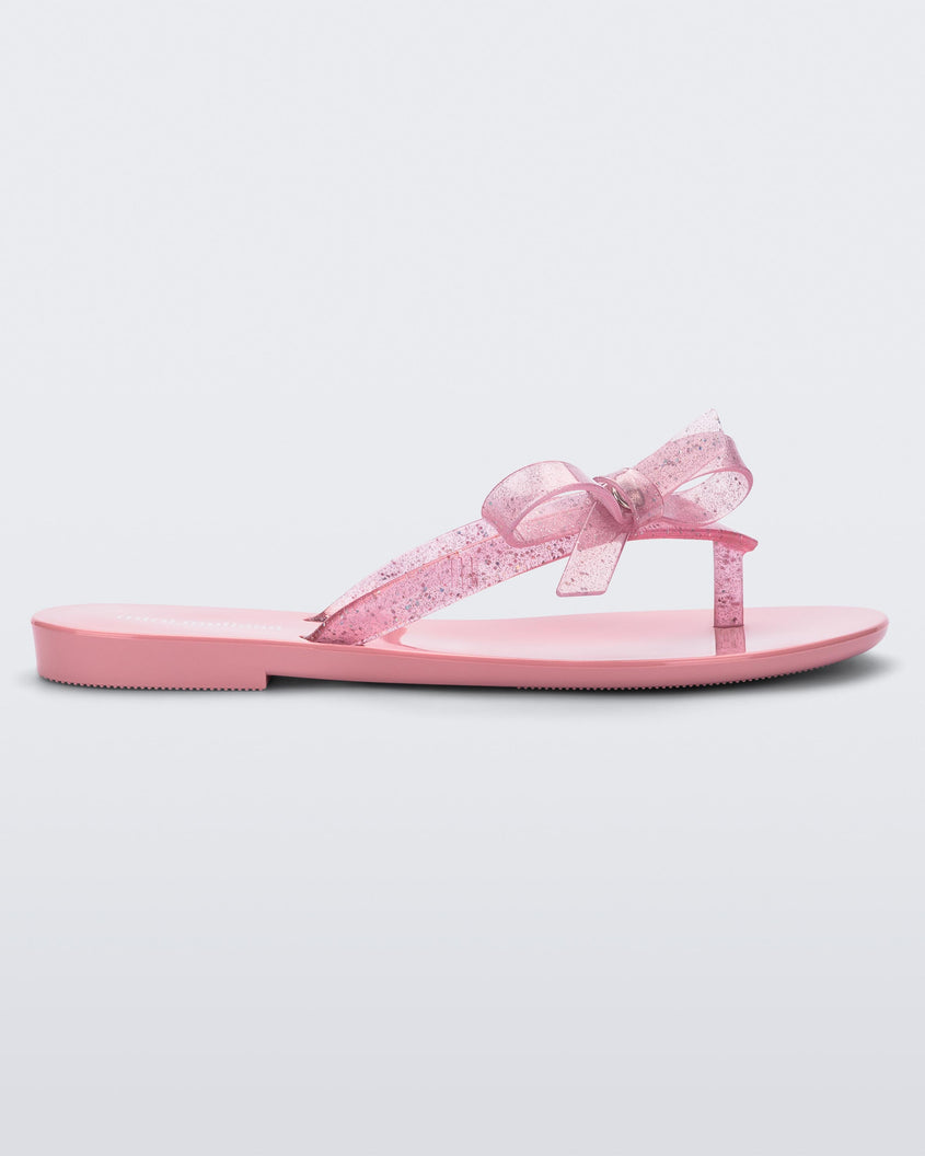 Side view of a Pink/Glitter Pink Mini Melissa Harmonic Sweet flip flop with a pink sole, pink glitter straps with a bow on top.