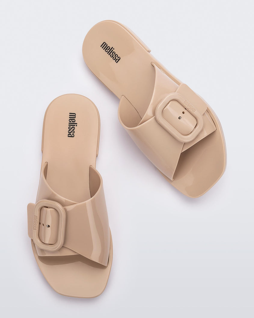 Top view of a pair of Beige Melissa Lislie slides with a buckle detail on the top strap.