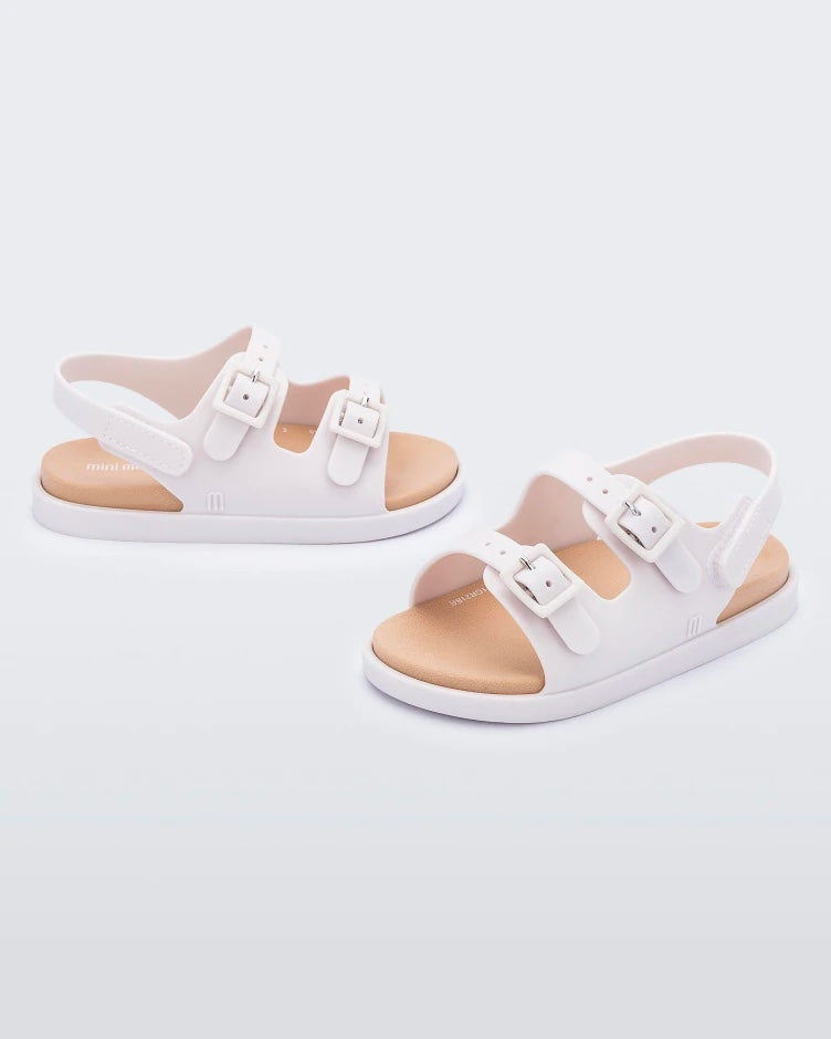 An angled front and side view of a pair of beige Mini Melissa Wide Sandals with a beige base, two buckles on top and an ankle strap.
