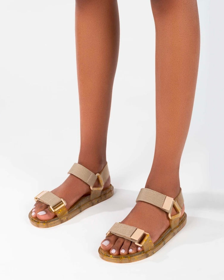 Model's legs wearing a pair of Melissa Wide Papete sandals with transparent beige glitter sole and beige velcro straps.