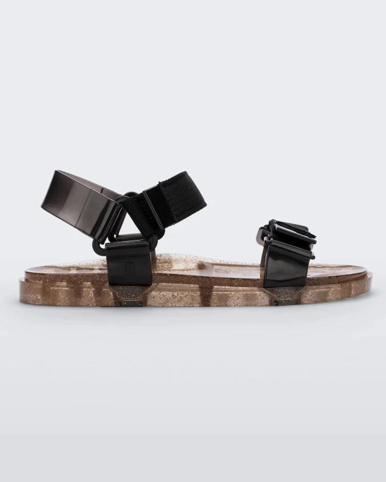 Side view of a Melissa Wide Papete sandal with transparent gold glitter sole with black velcro straps 