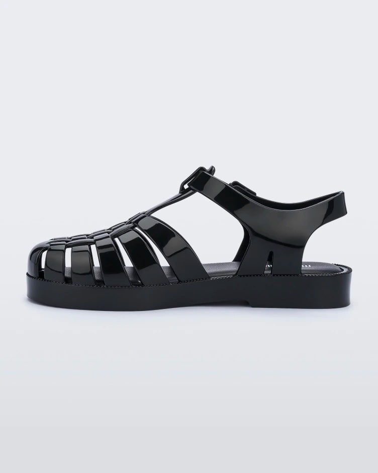 An inner side view of a black Mini Melissa Possession sandal with several straps and a black base.