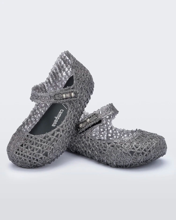 An angled top and side view of a pair of black glitter Mini Melissa Campana flats with a snap strap for baby and an open woven texture, leaning on eachother.