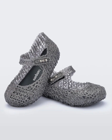 An angled top and side view of a pair of black glitter Mini Melissa Campana flats with a snap strap for baby and an open woven texture, leaning on eachother.